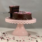 Port wine chocolate cake on cake stand with slice lifted