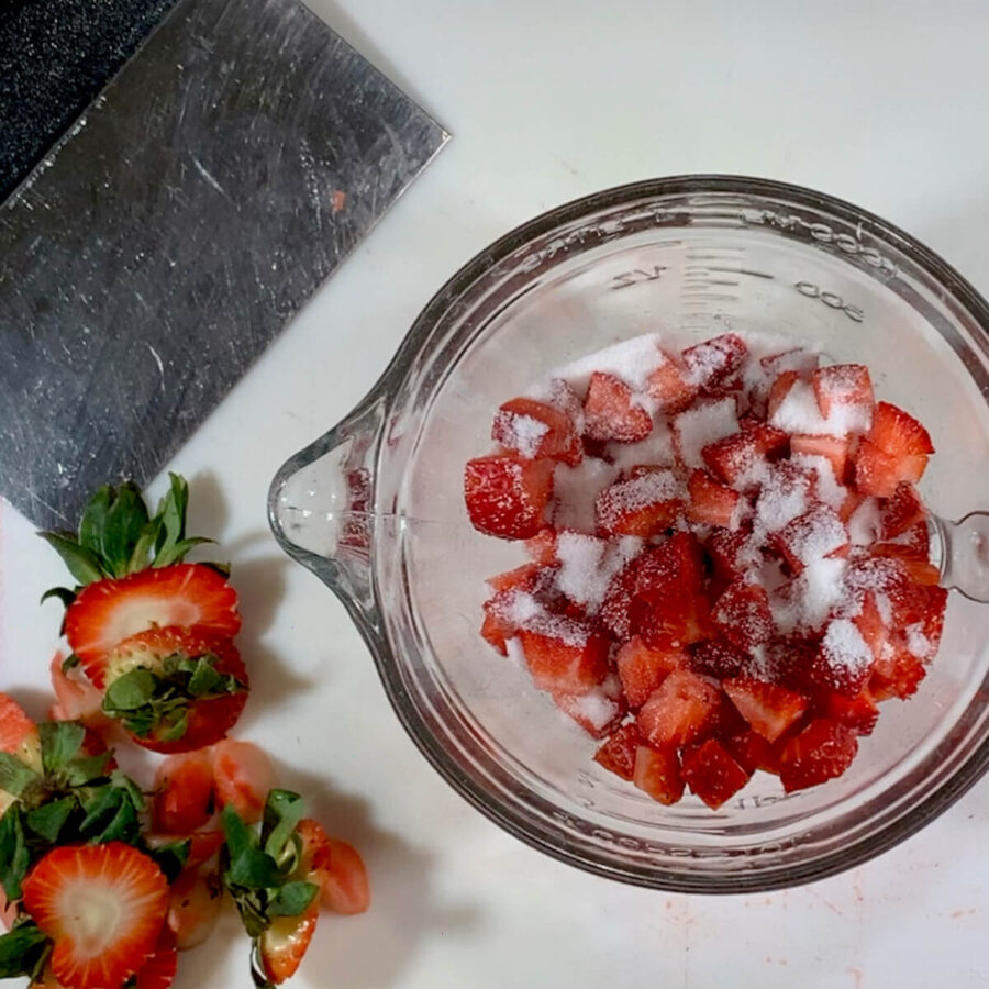 Chopped strawberries in a bowl sprinkled with sugar with strawberry tops to side