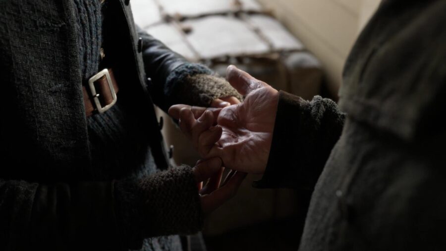 Close-up image of Claire holding Tom Christie’s injured hand. His hand resembles the shape of a claw due to tendon/nerve pain and injury