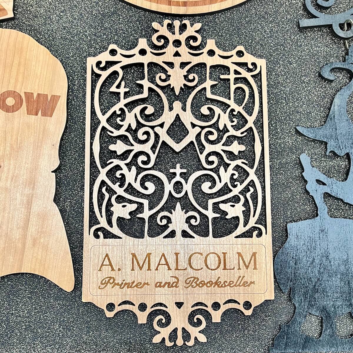 A laser cut wooden sign of the show's "A. Malcolm" printer's sign from STARZ series, Outlander, Season 3.